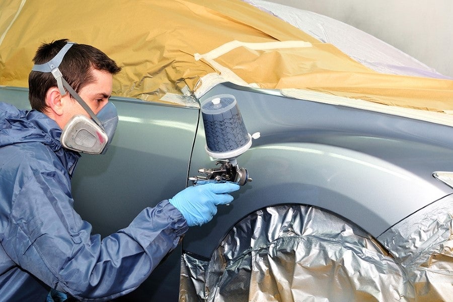 A person in protective gear spray paints a car fender.